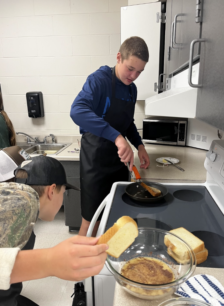 A student helps their partner check if their French Toast is done. 