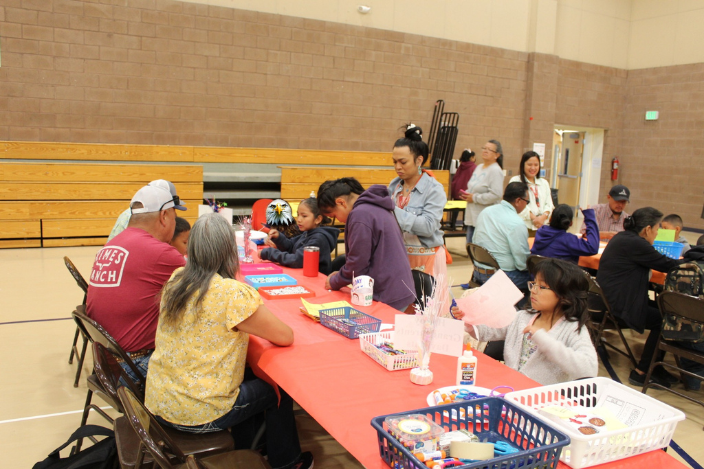 Ms. Westover showing families how to do the activity for grandparents day. Grandparents and students are sitting at the table during the activity.