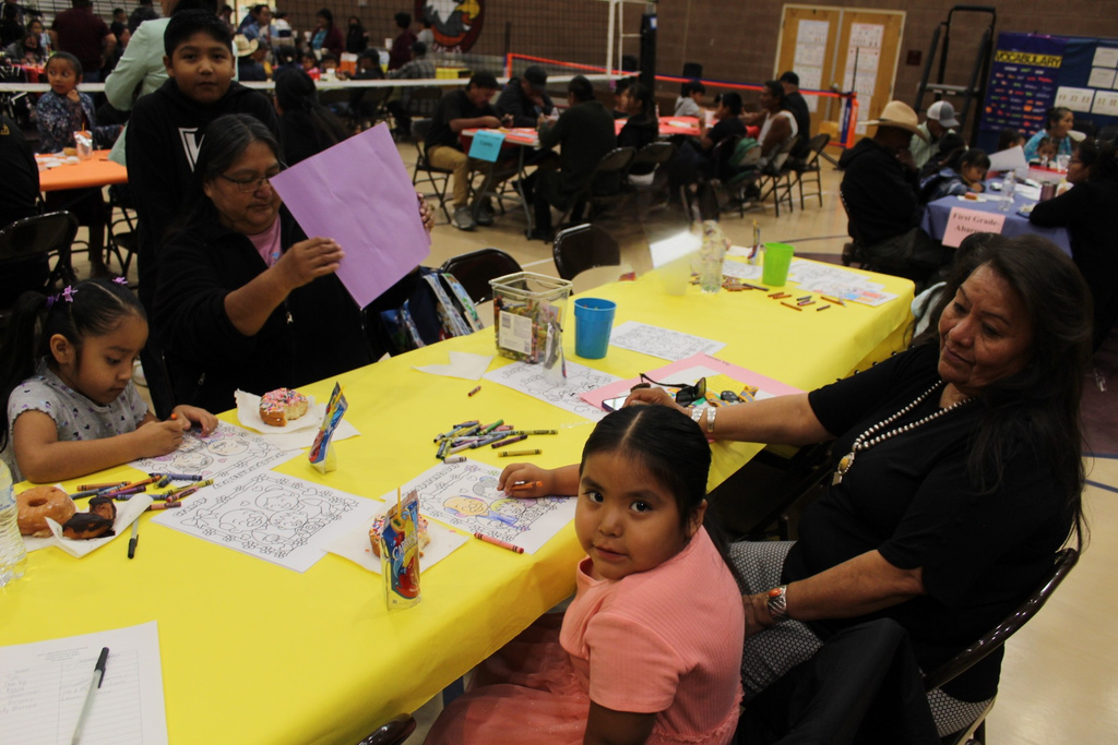 A grandma and her two grandchildren looking at the activity. A grandmother and her granddaughter coloring together.