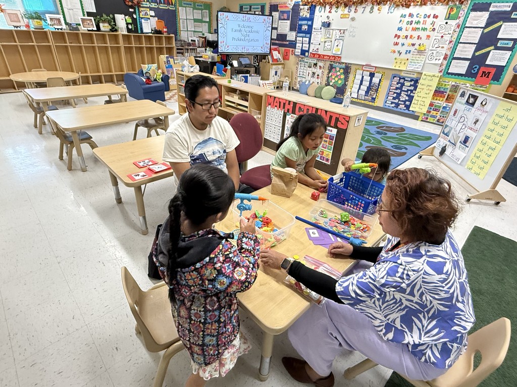 Father and daughters playing a game with the PreK teacher during family academic night. 