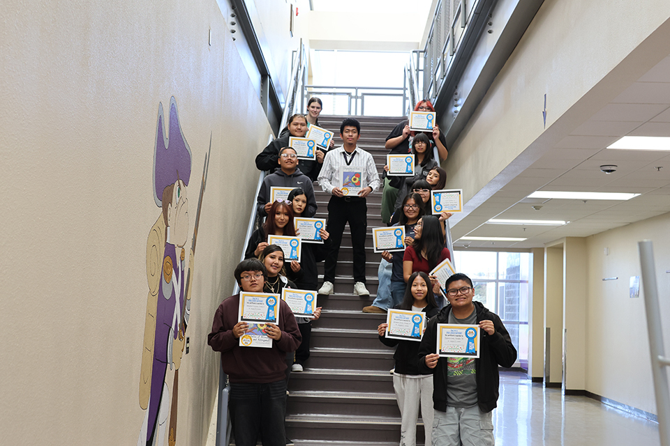 ELA students and teacher posing with their certificates lined up down a stairwell