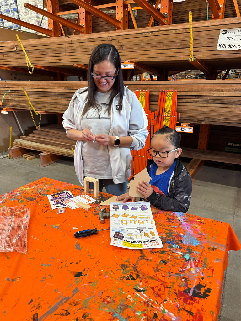 A woman and a child work on a craft at a table covered with orange fabric.
