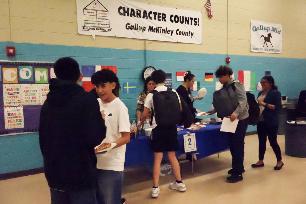 A group of people gather around a table with food, with banners on the walls and flags.