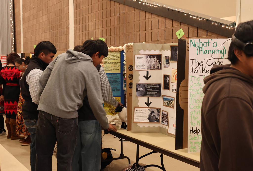 People examine a display at a table, showing a collage of images and text. Background has brick walls.