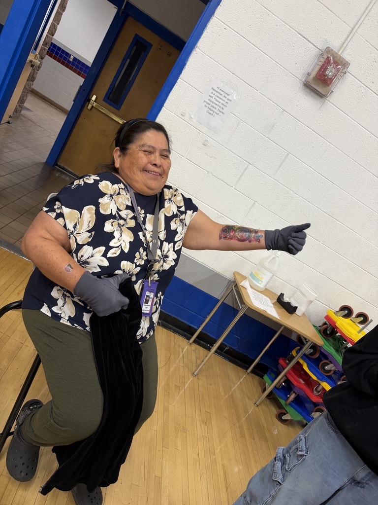 A woman wearing a blue floral shirt, gloves, and pants stands in a room with wooden floors.