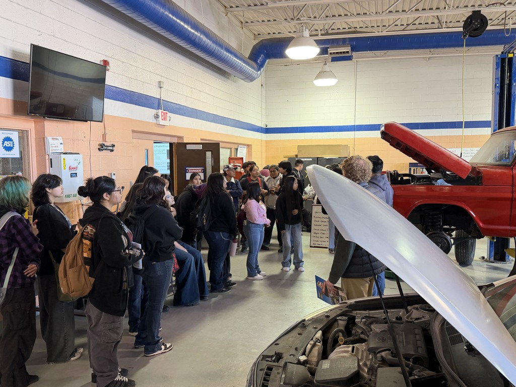 20 students in a mechanic shop listening to a speaker