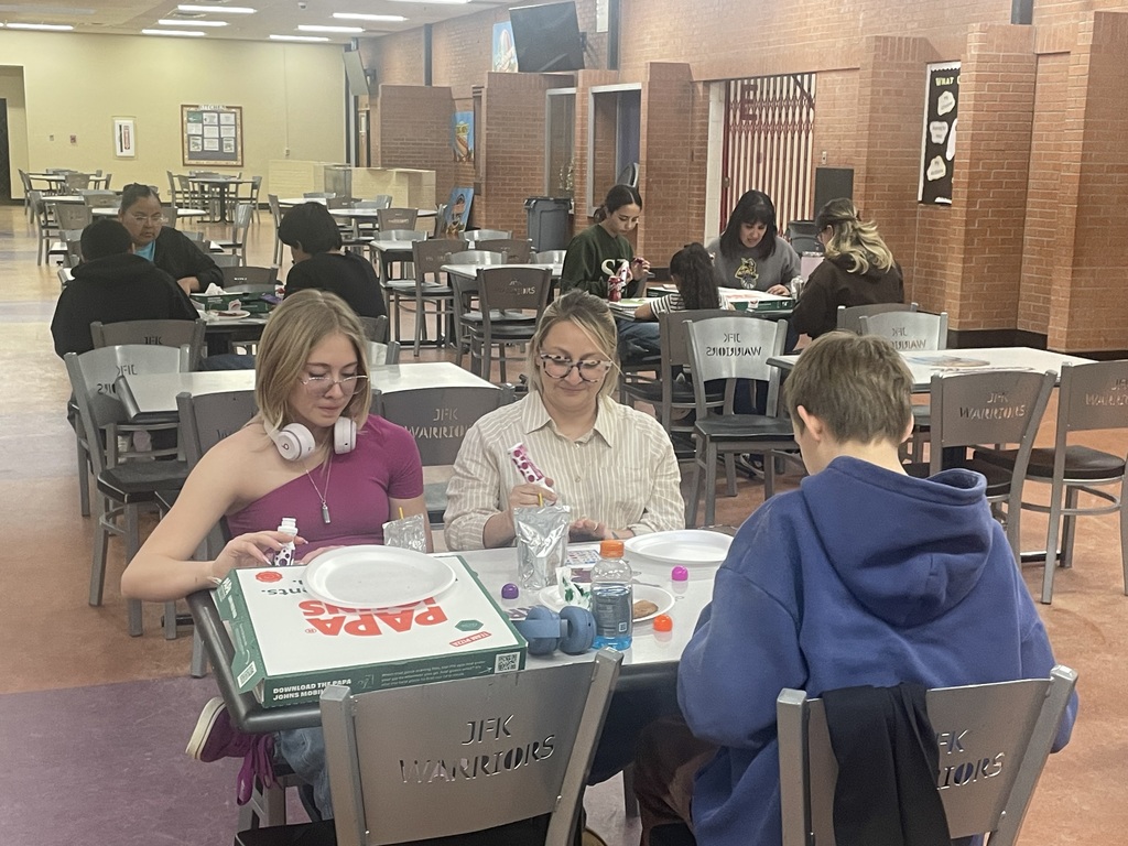 Three people sitting at a table in a dining area, one wearing glasses, another in a purple shirt, and the third in a blue hoodie.