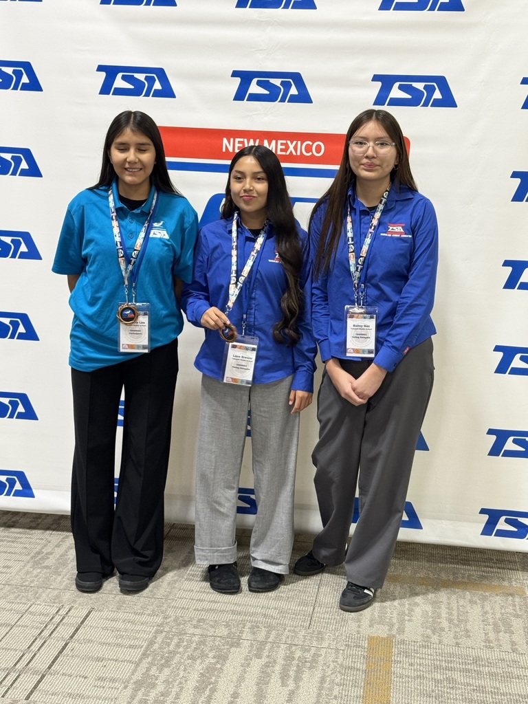 Three women in blue shirts and lanyards pose for a photo in front of a white banner.