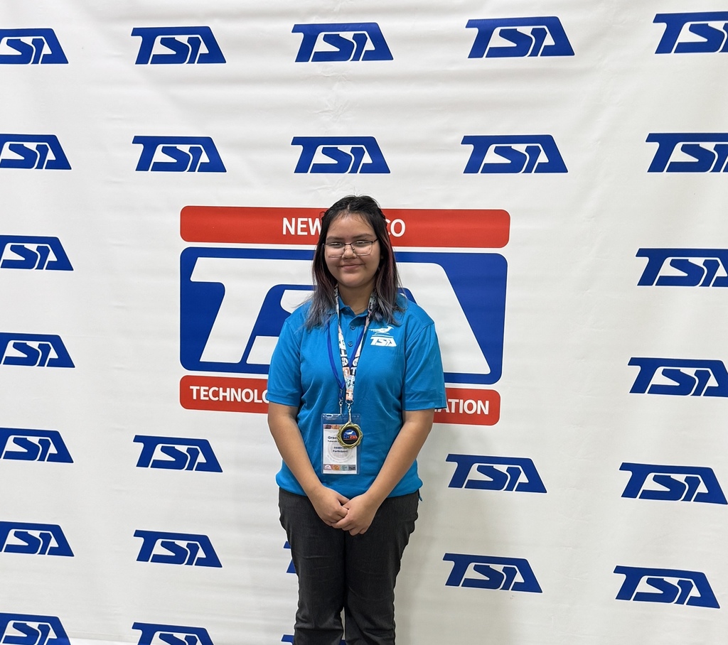 Person in a blue shirt with "NEW TO" on it stands in front of a white backdrop with blue letters.