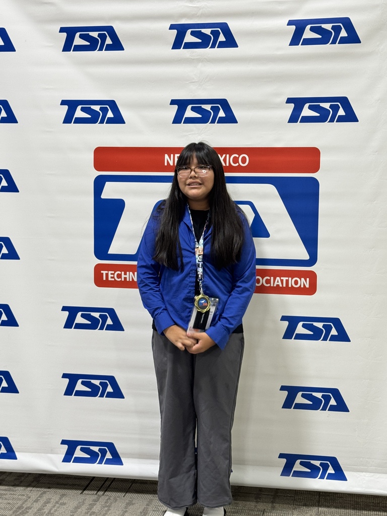 A person stands in front of a banner, holding a trophy. The banner features "TSA TECHNICIAN" in red letters and multiple "TSA" logos.