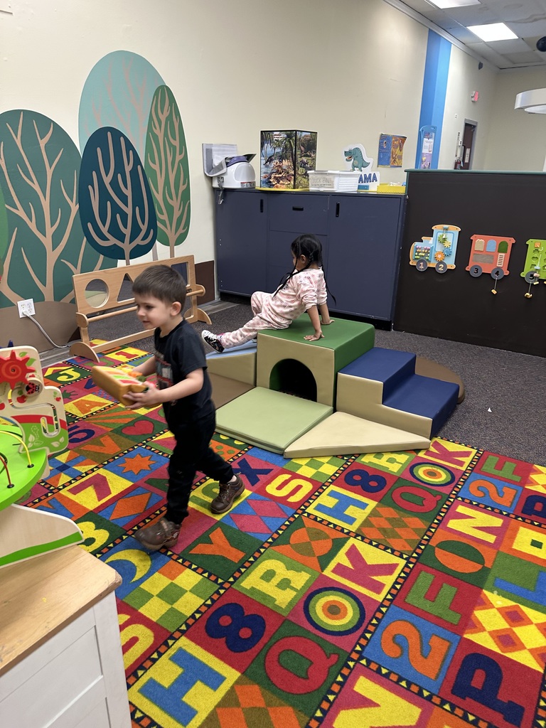 Two children play in a colorful play area with alphabet tiles and interactive features. Bright, playful decor.