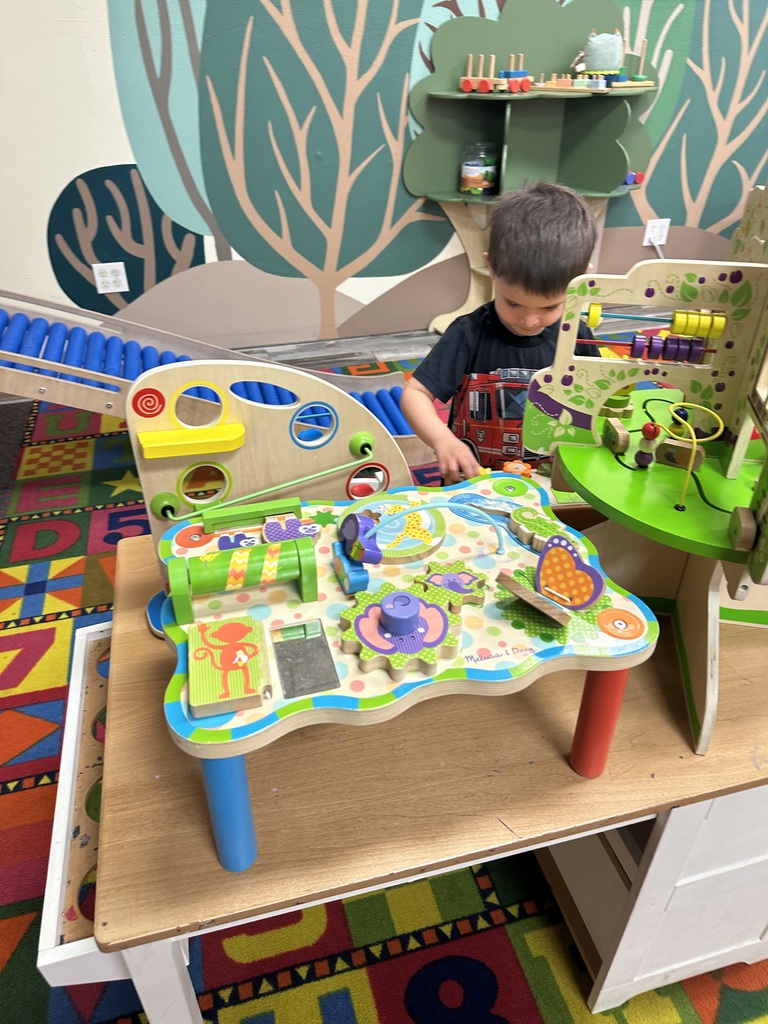 A child playing with a colorful wooden puzzle board on a table in a playroom.