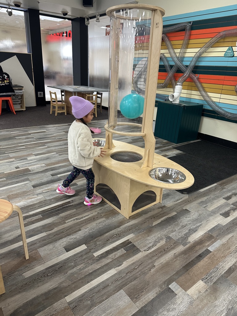 A young child plays with a colorful ball machine in a brightly colored room with wooden floors.