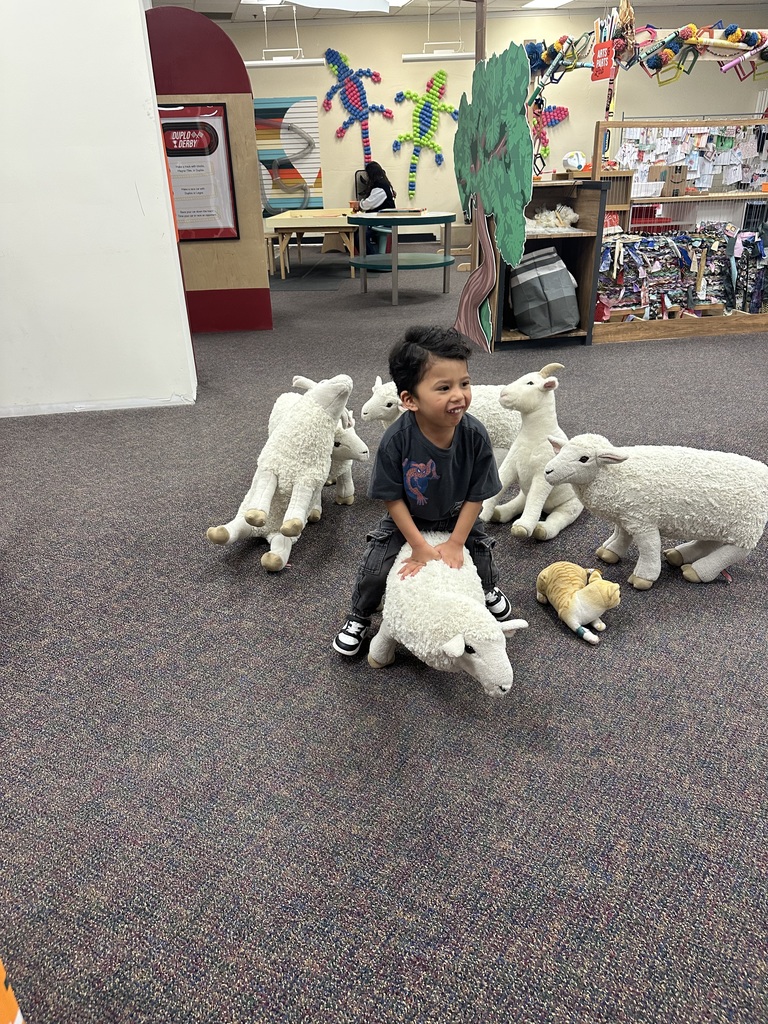 A young child plays with plush animal toys in a room with bookshelves and a table.
