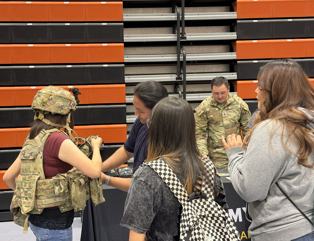 A group of people in military and civilian clothing interact at a table in an auditorium.
