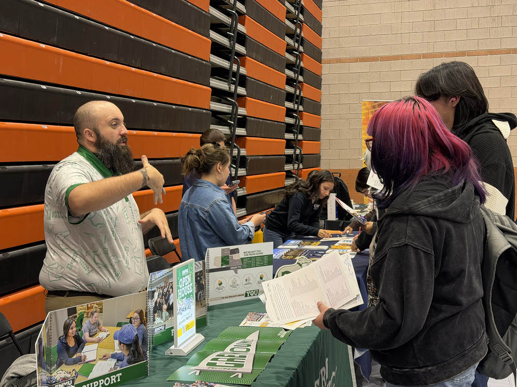 People gather at a table with brochures in a gym with orange and black walls.