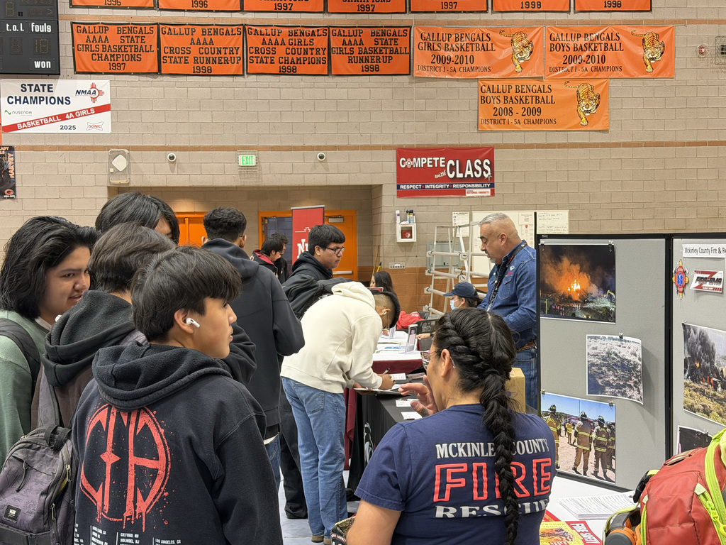 Students in a gym with banners, one wearing a firefighter shirt, while others in hoodies.