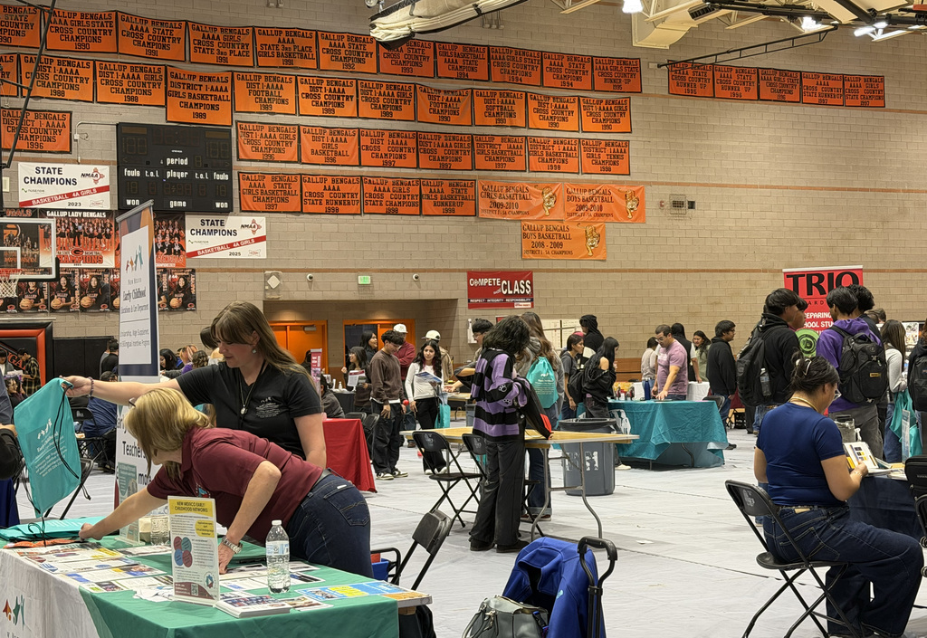 A gym hosts a job fair with tables and booths. People gather around tables, and some sit in chairs.