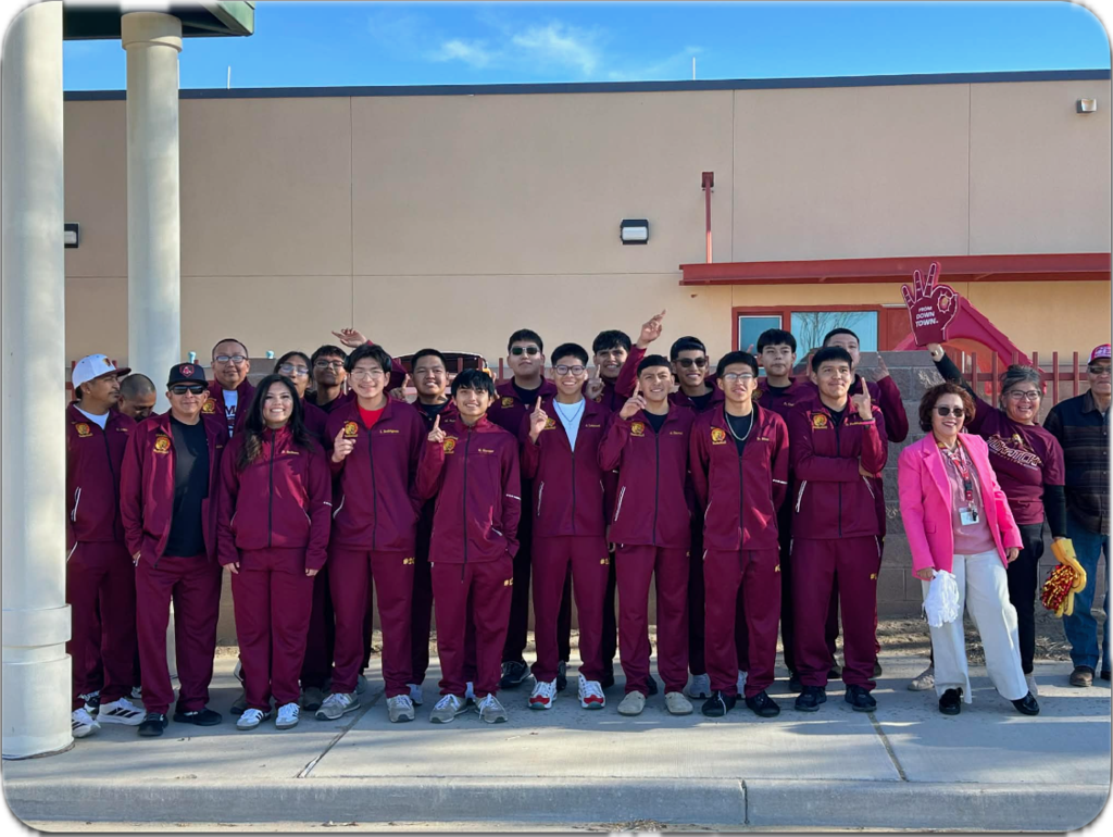 A group in maroon uniforms poses in front of a building. Some make hand gestures.