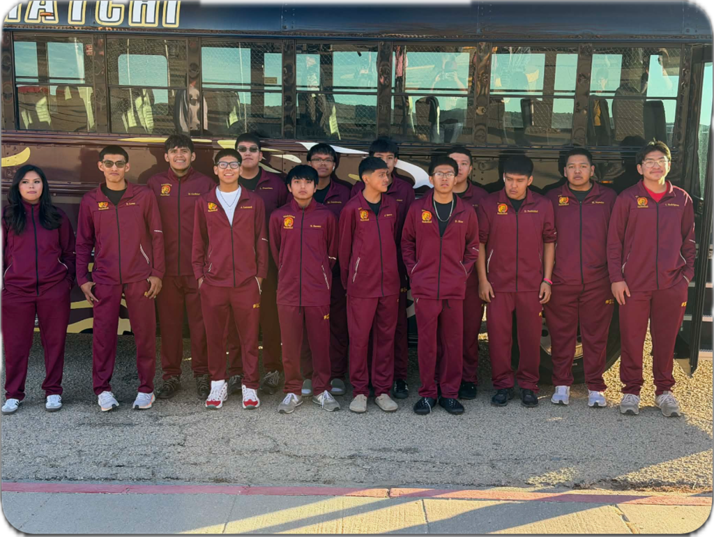 A group of people in matching maroon uniforms stand in front of a bus on a sunny day.