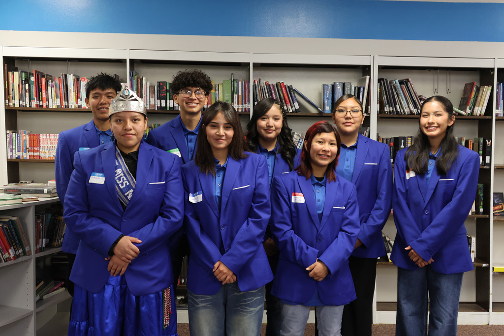 A group of students in matching blue blazers pose for a photo in a library.
