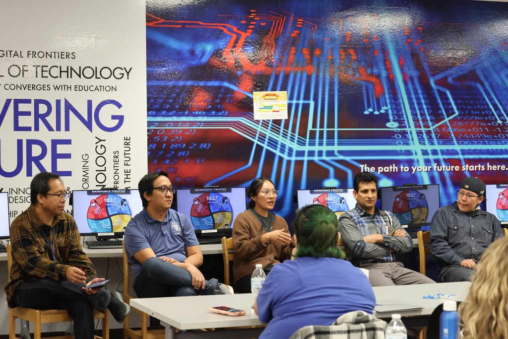 Several people sit around a table, possibly during a panel discussion, in front of a large backdrop.