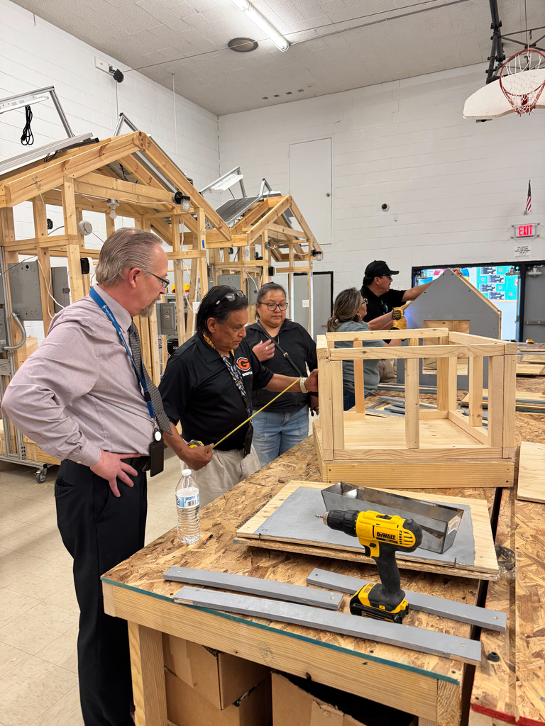 A group of people in a workshop. One person is measuring a wooden structure with a tape measure.