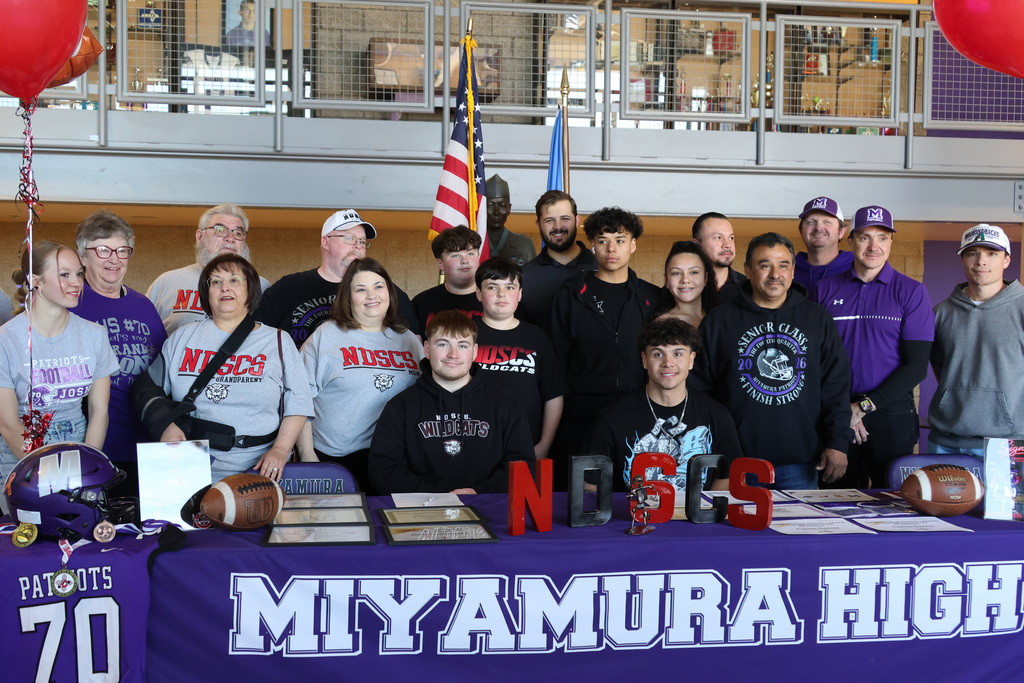 Group photo at Miyamura High. People stand behind a banner with red balloons and a table with footballs and a flag.