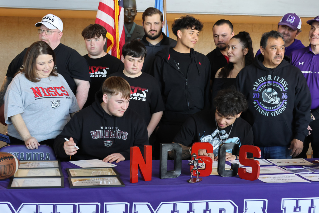 Group of people posing behind a table with a football, NOCS letters, and documents.