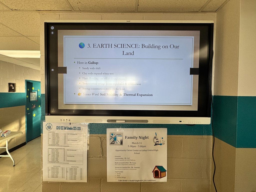 Monitor displays a slide titled "Earth Science: Building on Our Land". Two papers on a wall, one titled "Family Night".