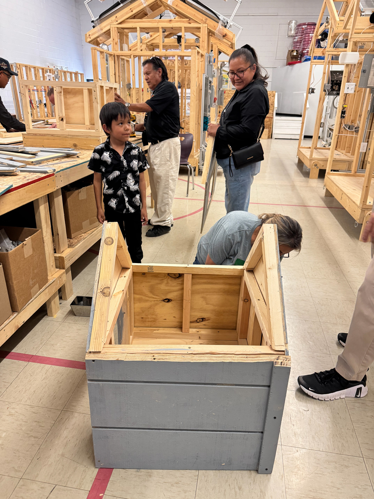 A group of people work on a wooden structure in a workshop. They are standing or bending over a wooden box.