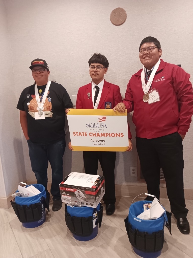 Three individuals stand with medals around their necks. One holds a box labeled "SkillUSA State Champions Carpentry."