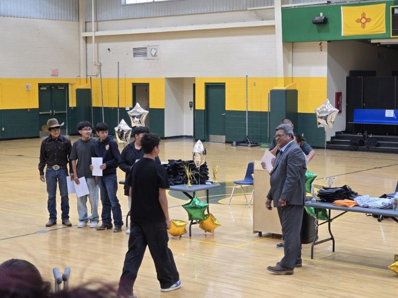 A group of people in a gymnasium. Some are standing, and others are walking. Tables with items are set up.