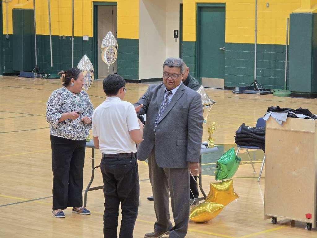 A man in a suit stands with a woman and a boy in a white shirt in a gym.