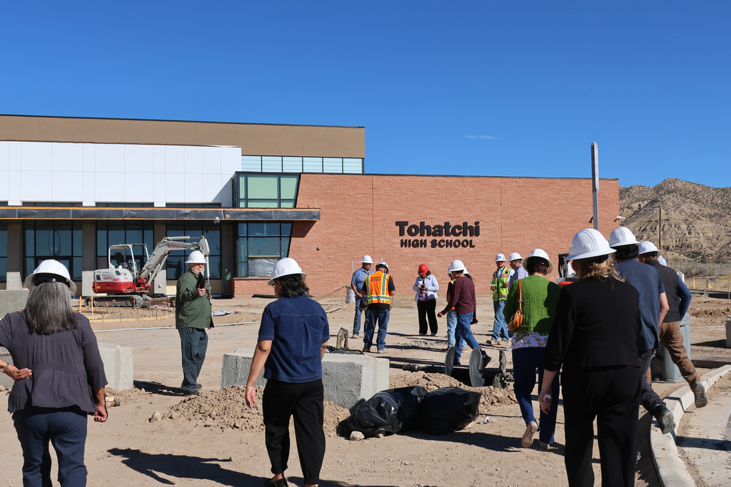 People on a construction site in front of a building that has a sign that reads "Tohatchi High School".