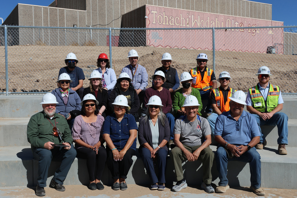 A group of individuals in hard hats sit on a concrete step in front of a building.
