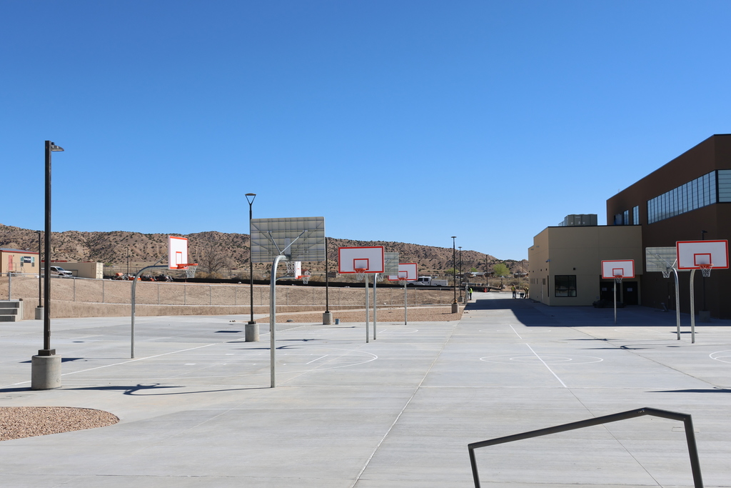 An outdoor basketball court with empty baskets, a building with windows, and a clear blue sky.