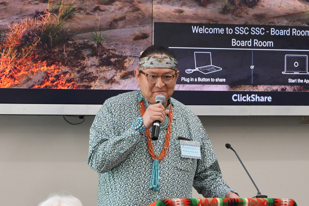 A man in traditional native jewlery holds a microphone