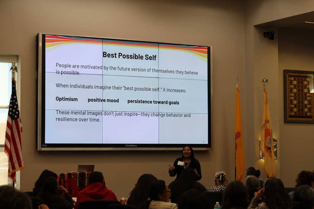 woman is presenting a presentation in from of an audience. They screen reads "Best Possible Self". 