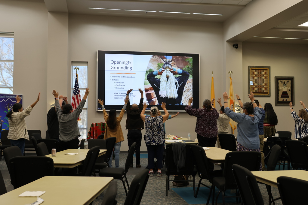 an audience engages in an activity by standing up and holding both arms in the air 