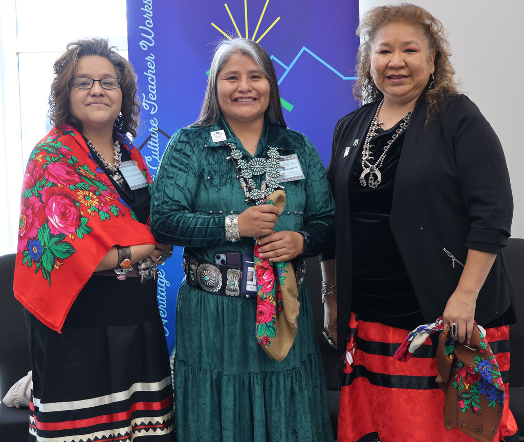 Three women stand together for a picture, each of them is in traditional native clothing and jewelry
