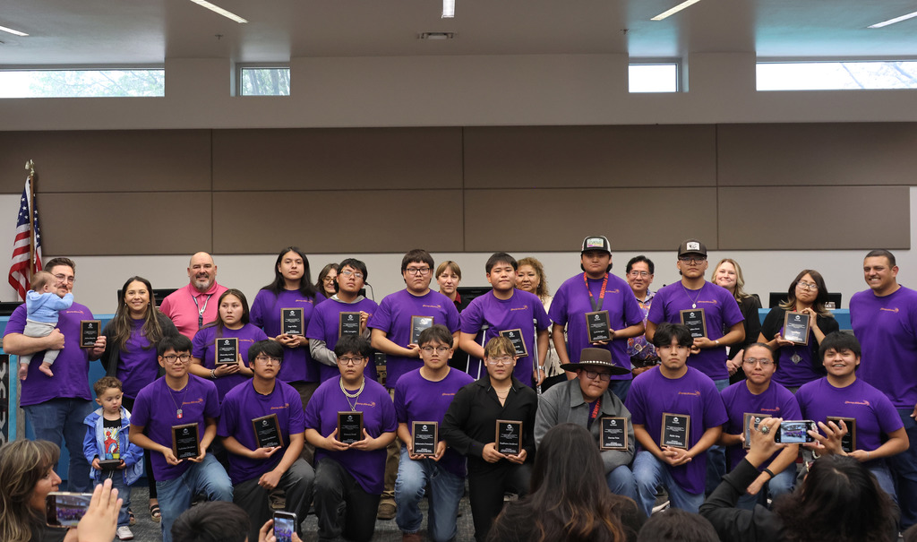 A group of people in purple shirts pose for a photo in a room with an American flag.