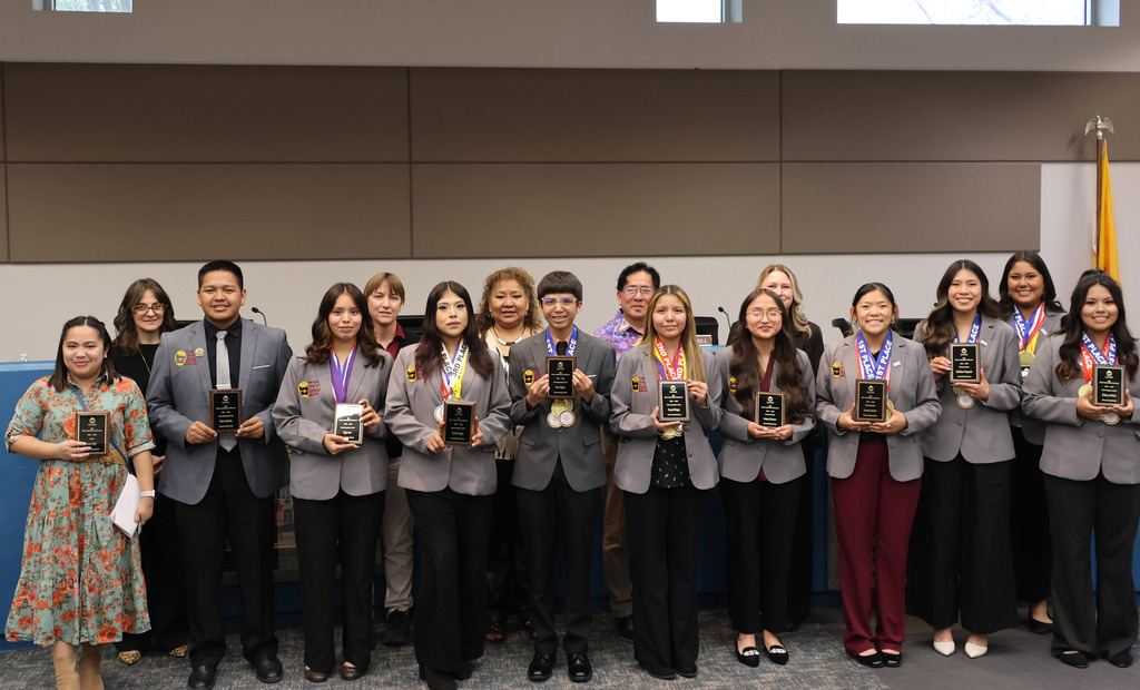 A group of individuals stands in two rows, smiling and holding awards, likely celebrating an achievement.