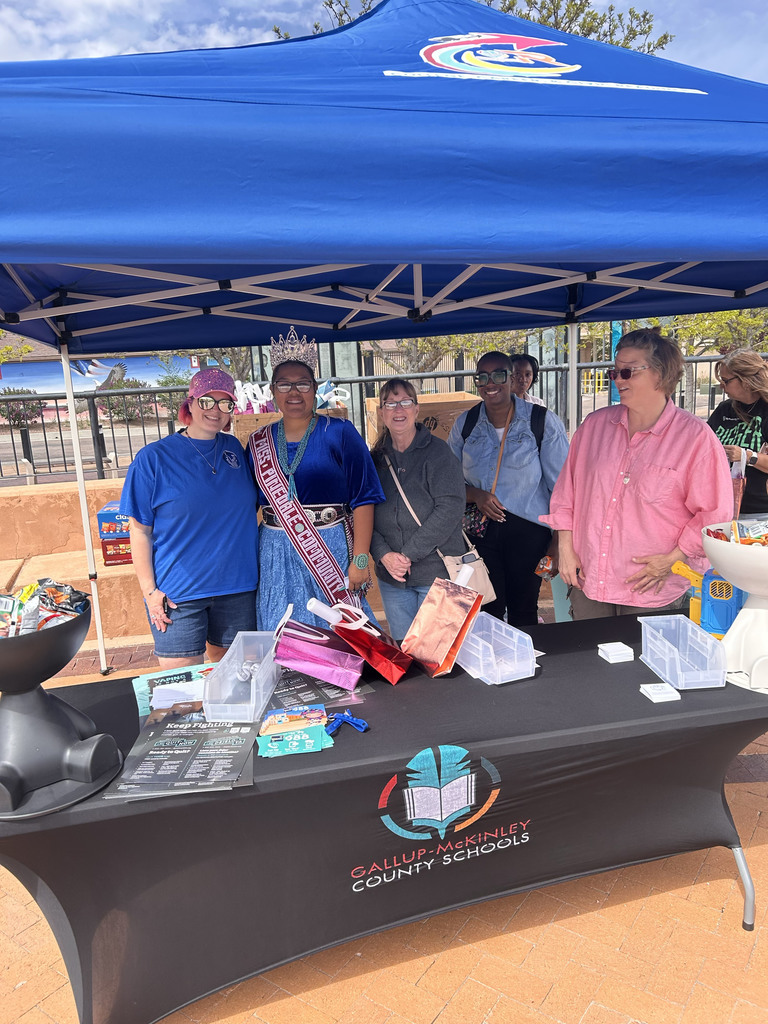 People under a tent with a banner. A table displays items, including bags and books.