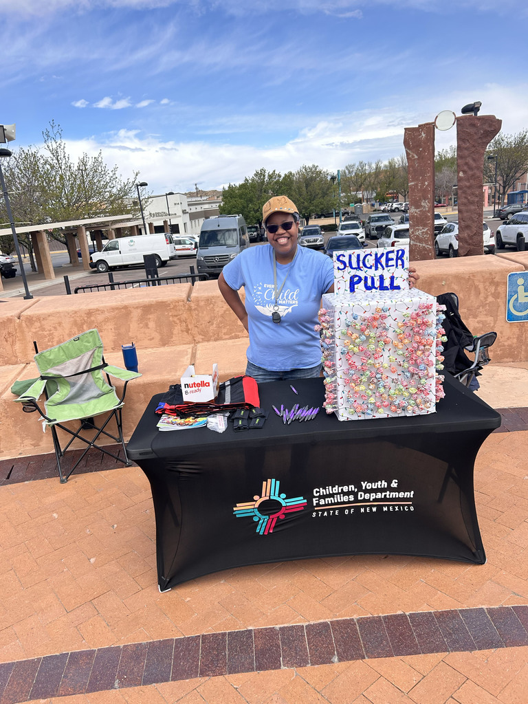 Person in blue shirt and hat standing behind a table. Sign reads "Sucker Pull" with a big candy bin. Green chair on the left.