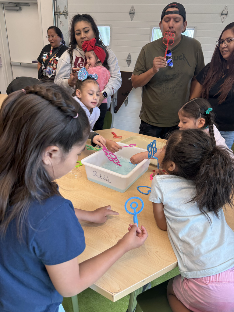 Several children and adults sit around a table, engaging in play with water and colorful toys.