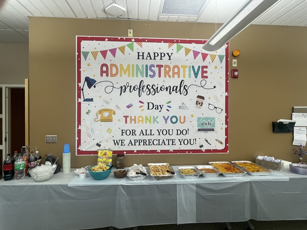 A room with a table covered in food. A sign on the wall says "Happy Administrative Professionals Day."
