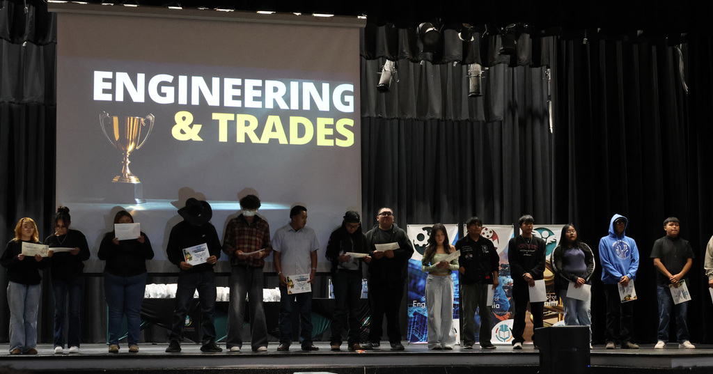 People holding certificates stand on a stage under a large screen with "Engineering & Trades" on it.