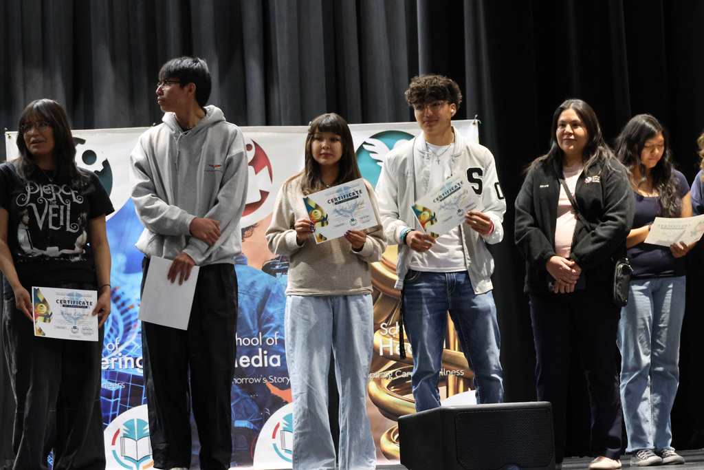 Several people on a stage, holding certificates. A banner with text and a musical horn behind them.