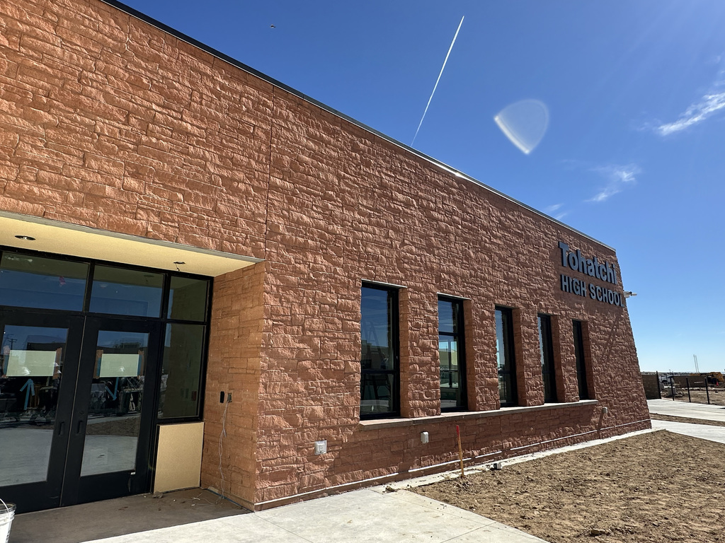 A building exterior with a brick facade, glass doors, and windows. Blue sky and clouds in the background.